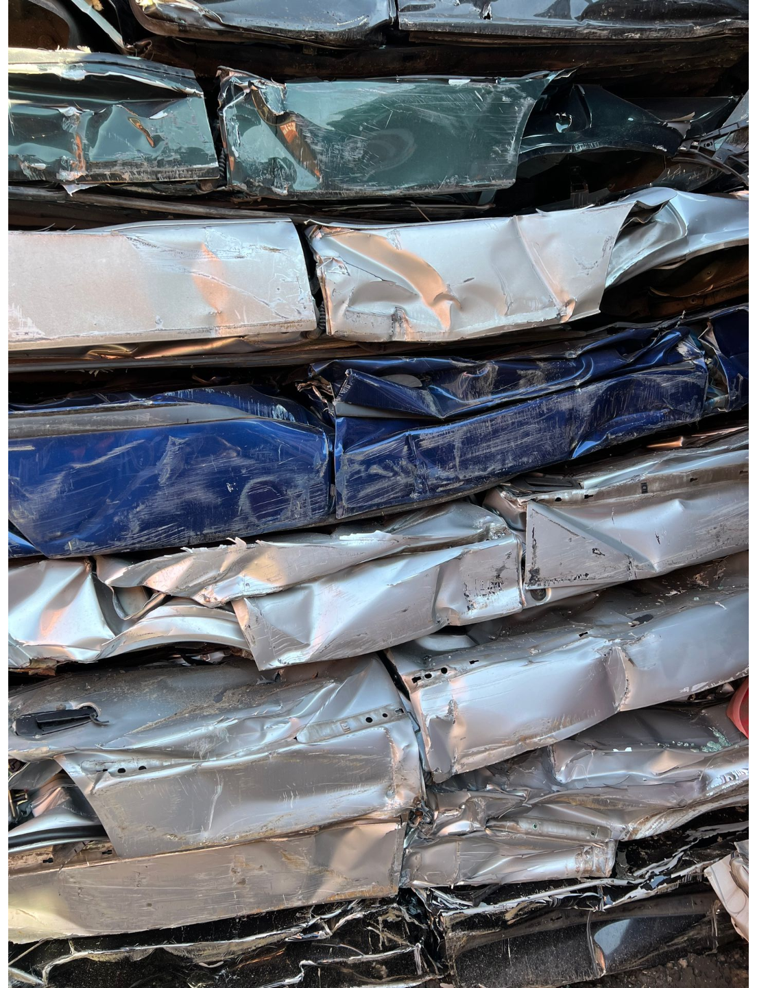Gestapelte, zerknitterte Päckchen aus Metallfolie in Silber, Blau und Schwarz, dicht aneinandergereiht in Reihen.