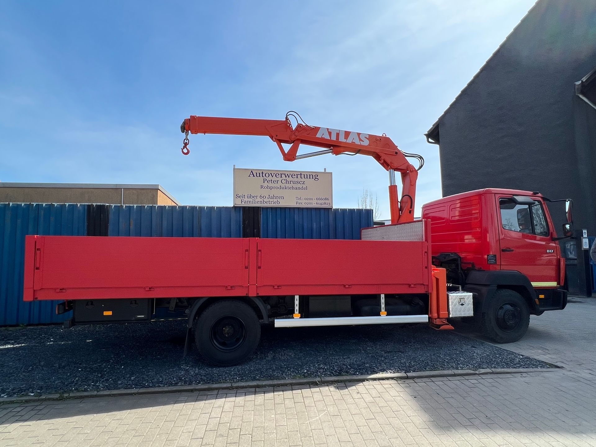 Ein roter Kranwagen parkt neben einem Gebäude und transportiert unter blauem Himmel eine lange rote Ladefläche.