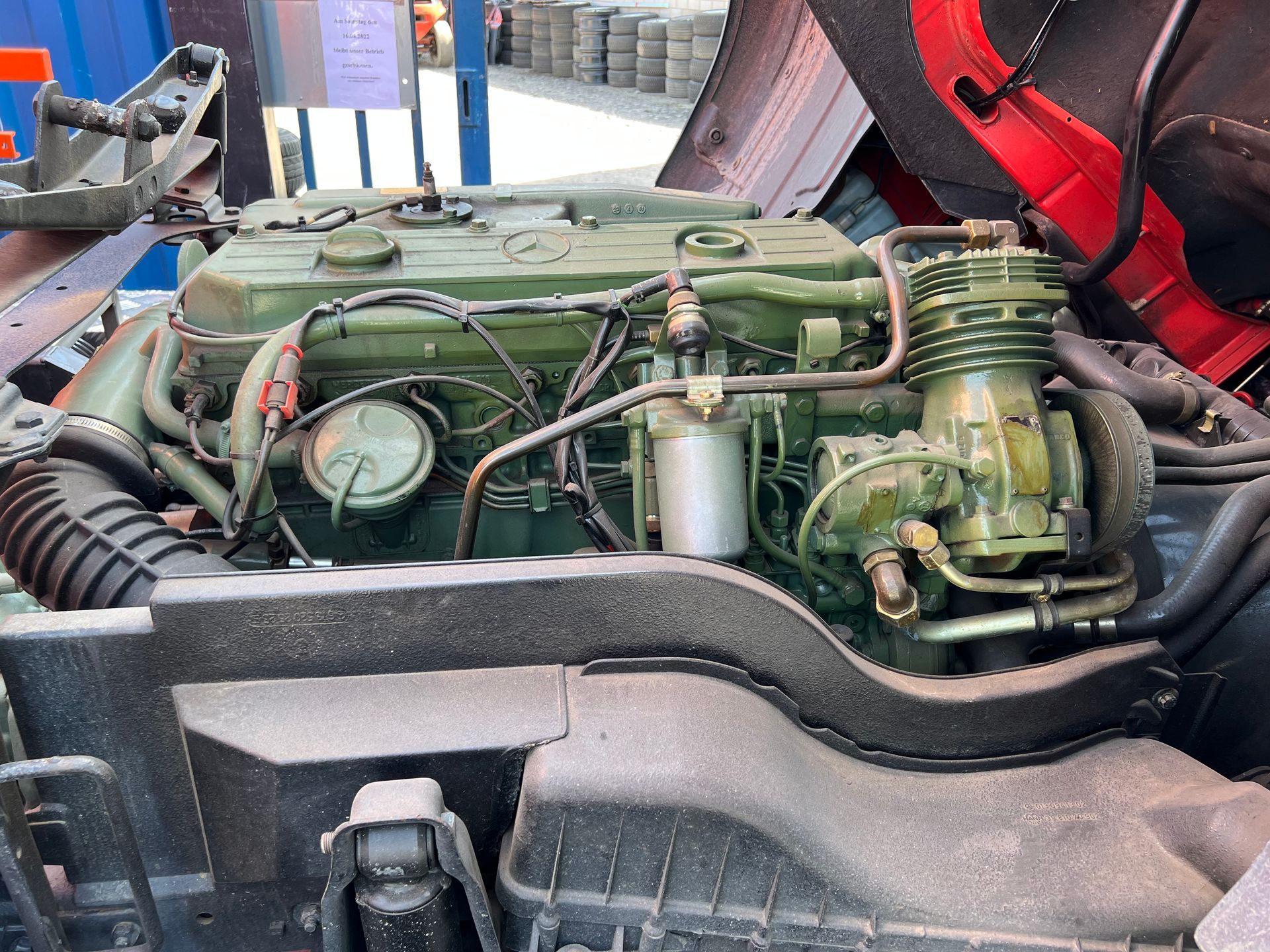 Offener Motorraum mit grünem Automotor und Schläuchen in einer Werkstatt