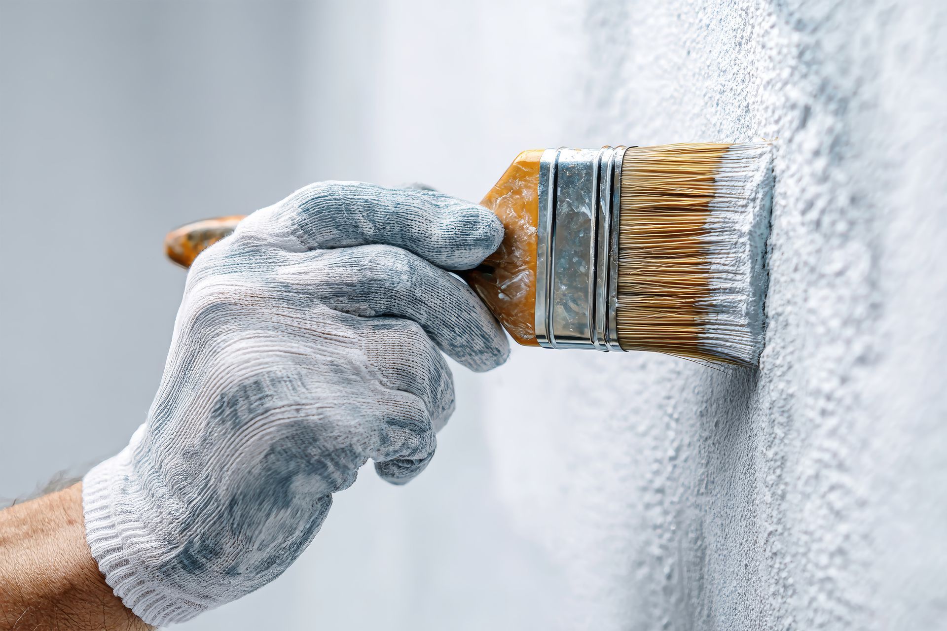 Application de peinture sur un mur avec un pinceau, par un peintre équipé de gants.