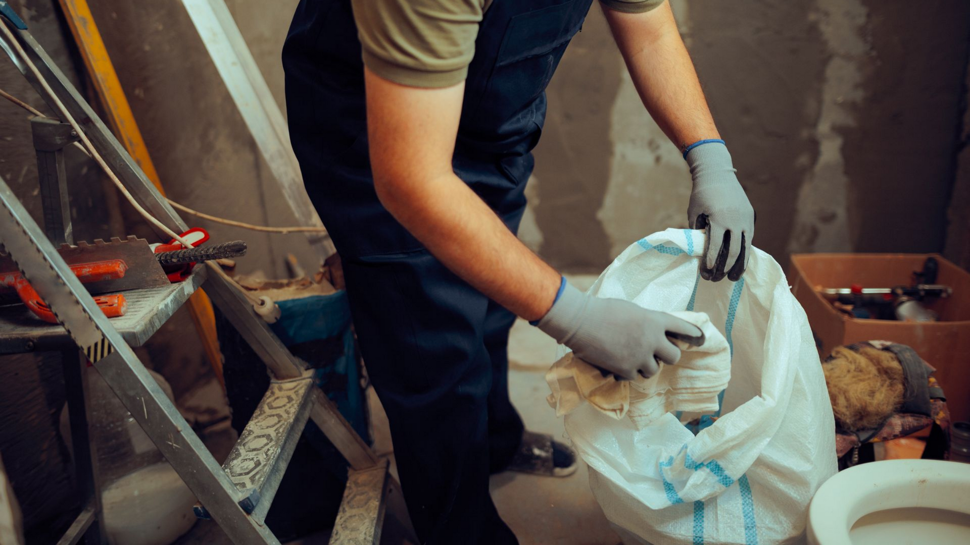 Personne portant des déchets dans un sac plastique sur un chantier.