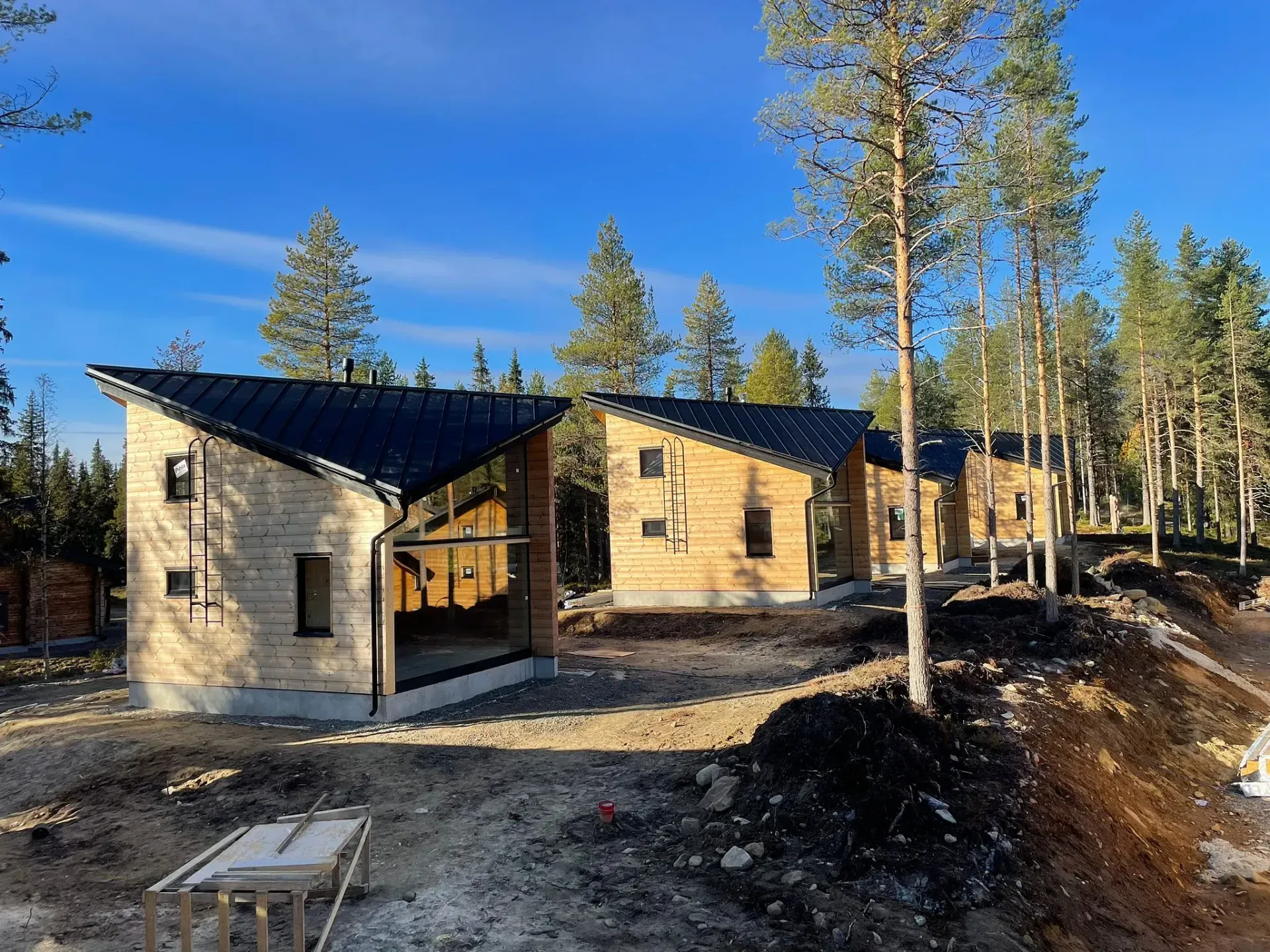 Rakenteilla olevia mustakattoisia puisia mökkejä metsämaisemassa.
