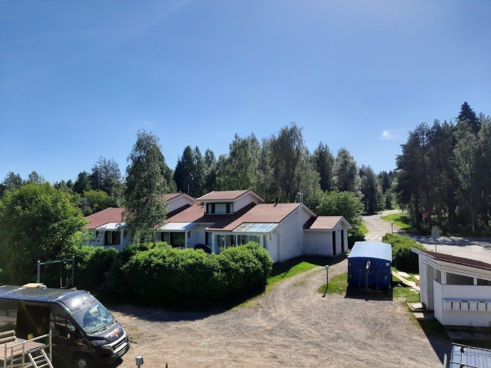 Valkoinen talo punaisella katolla, vihreiden puiden ympäröimänä aurinkoisena päivänä