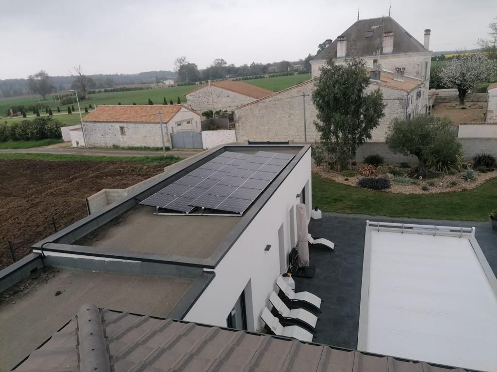 Vue aérienne d'un bâtiment moderne blanc doté d'un toit plat recouvert de panneaux solaires, à côté d'une piscine avec une couverture blanche.