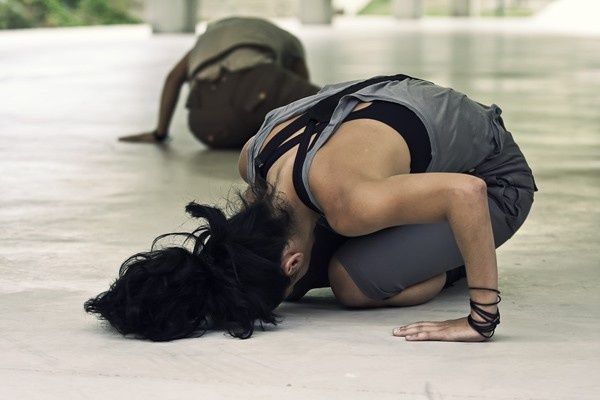 Una persona estaba agachada en el suelo, con la cabeza gacha, vestida de negro y con una mochila a la espalda.