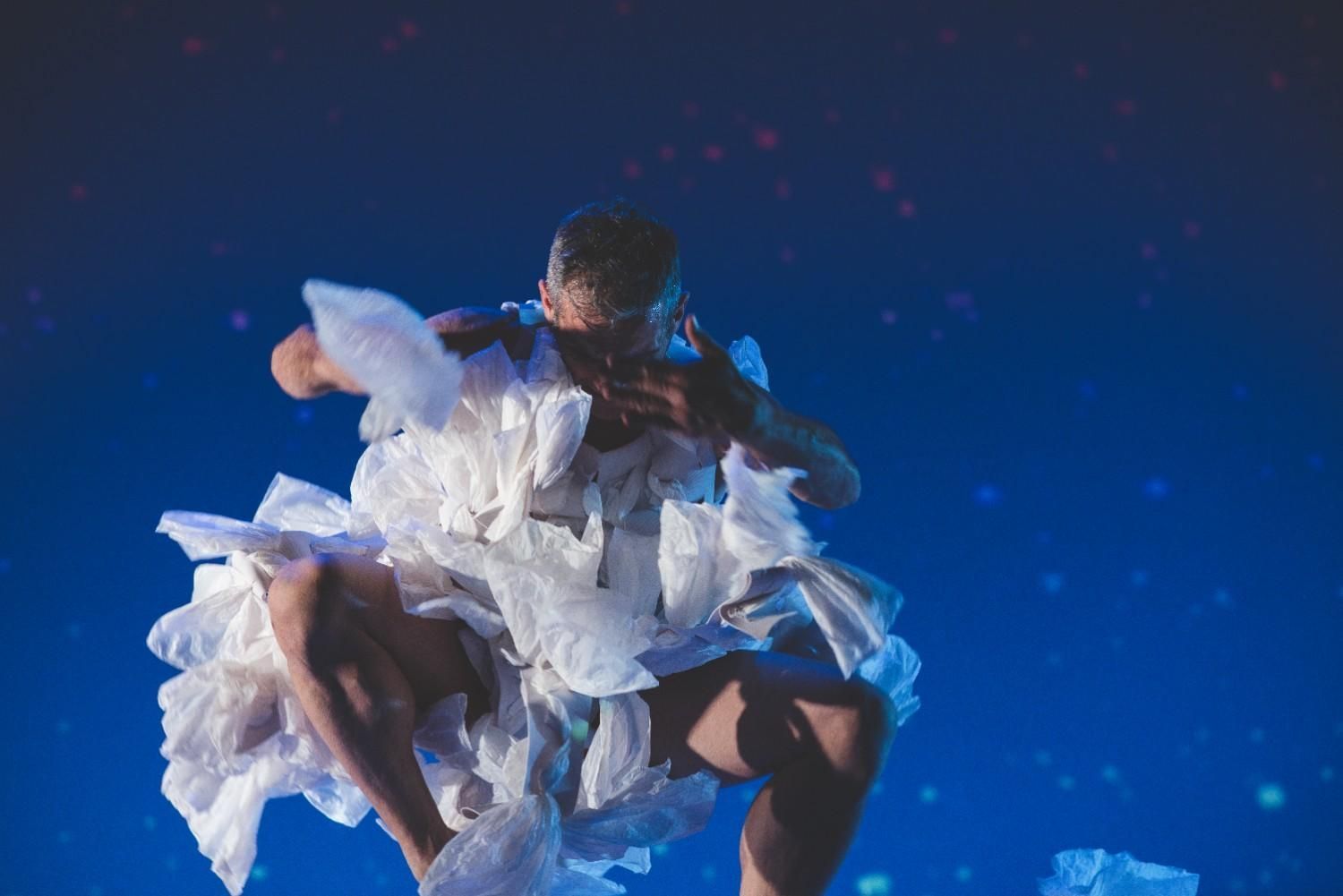 Bailarina con un vaporoso traje blanco saltando sobre un fondo azul en el escenario con luces que simulan estrellas.