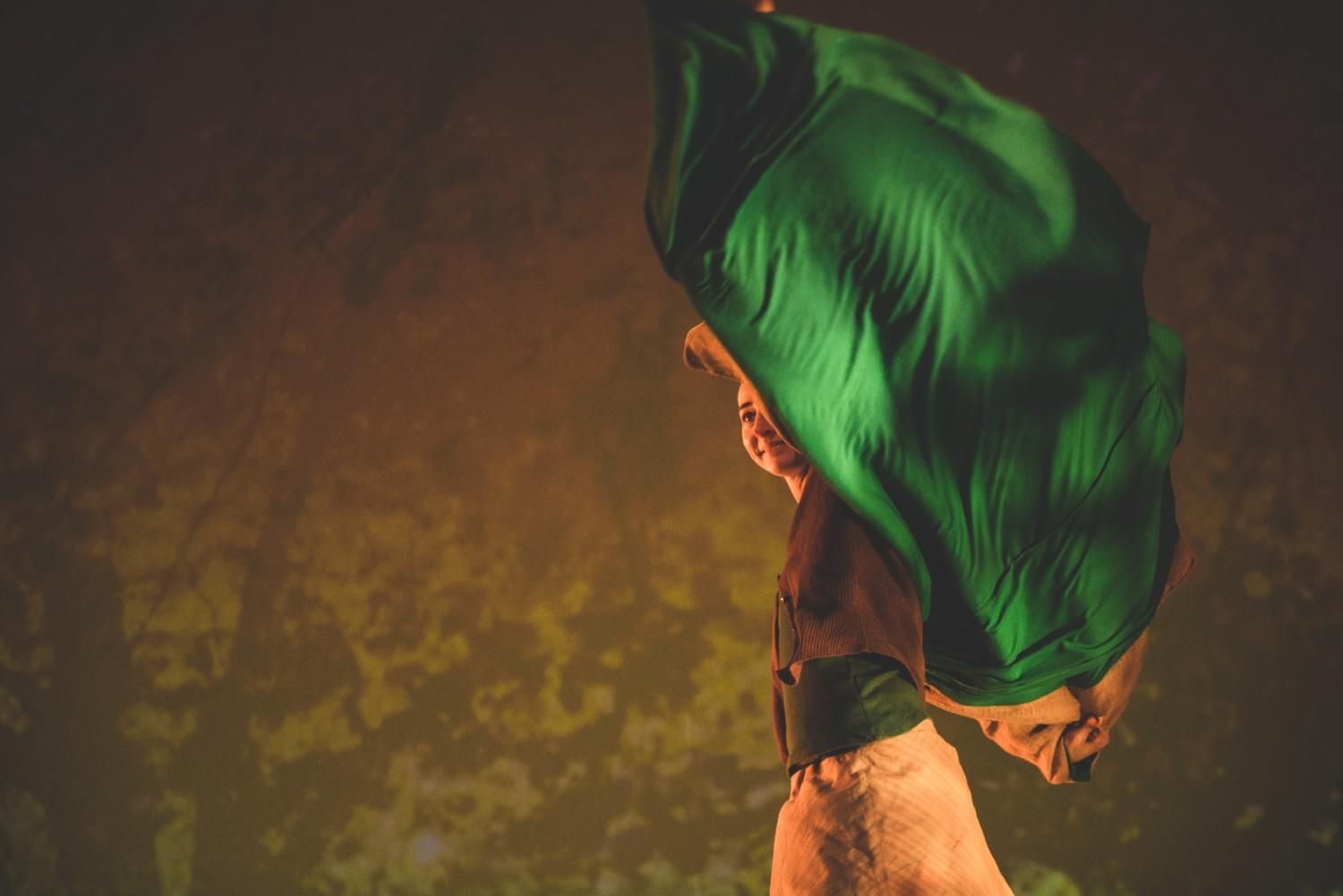 Tela verde drapeada sobre el brazo de una persona sobre un fondo oscuro de tonos cálidos.