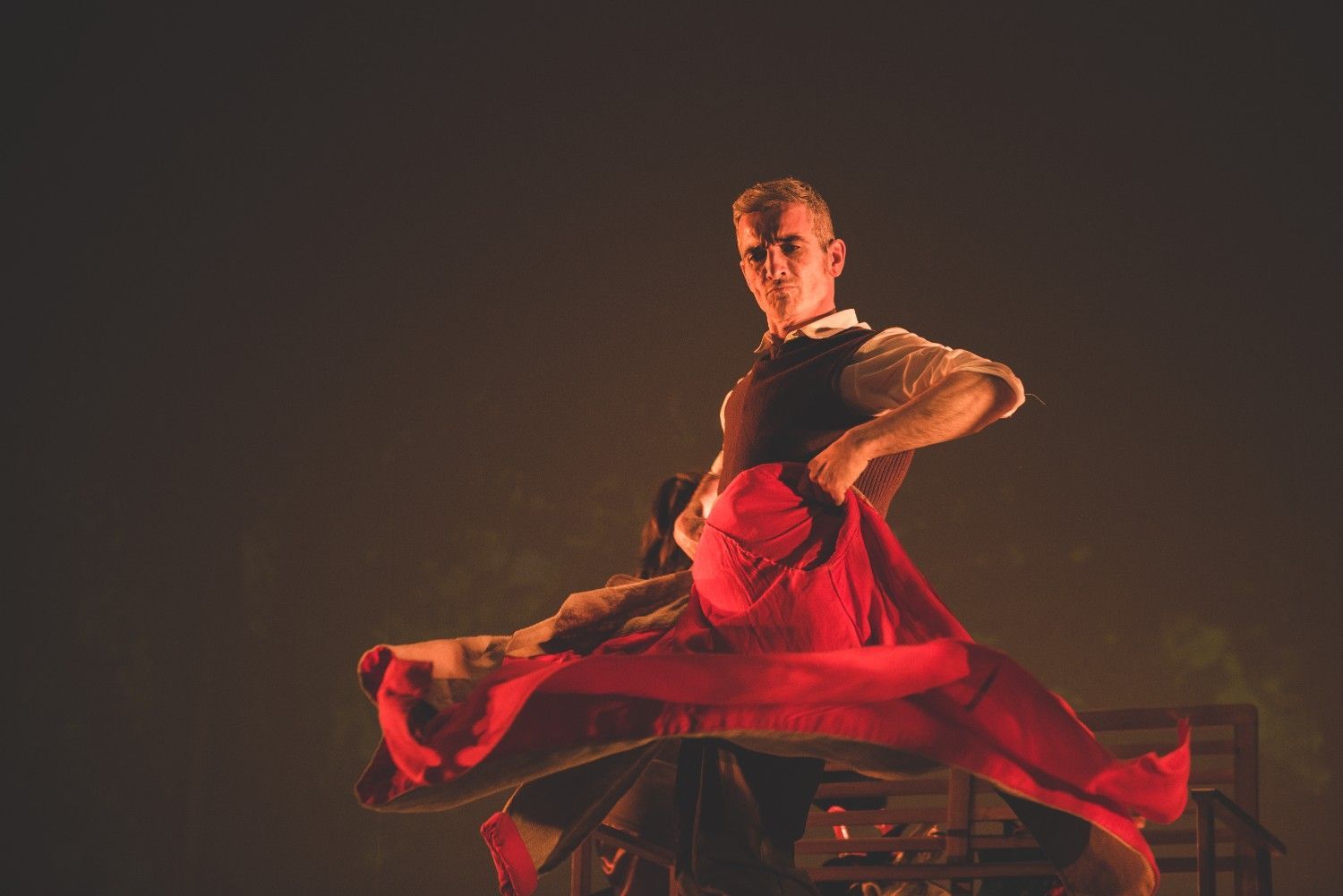 Una bailarina con un vaporoso traje rojo salta contra un telón de fondo oscuro.