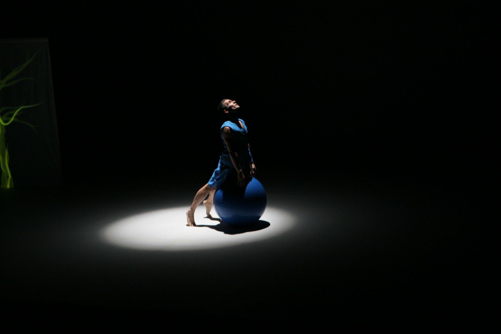 Una persona con un vestido azul sentada bajo un foco en una habitación oscura con un gato cerca.