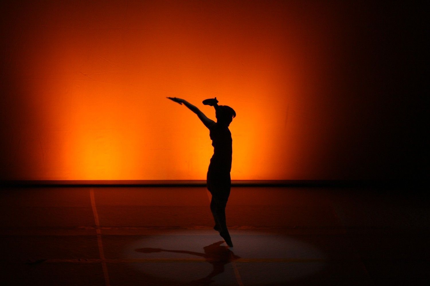 Bailarina en silueta sobre el escenario contra un fondo naranja brillante.