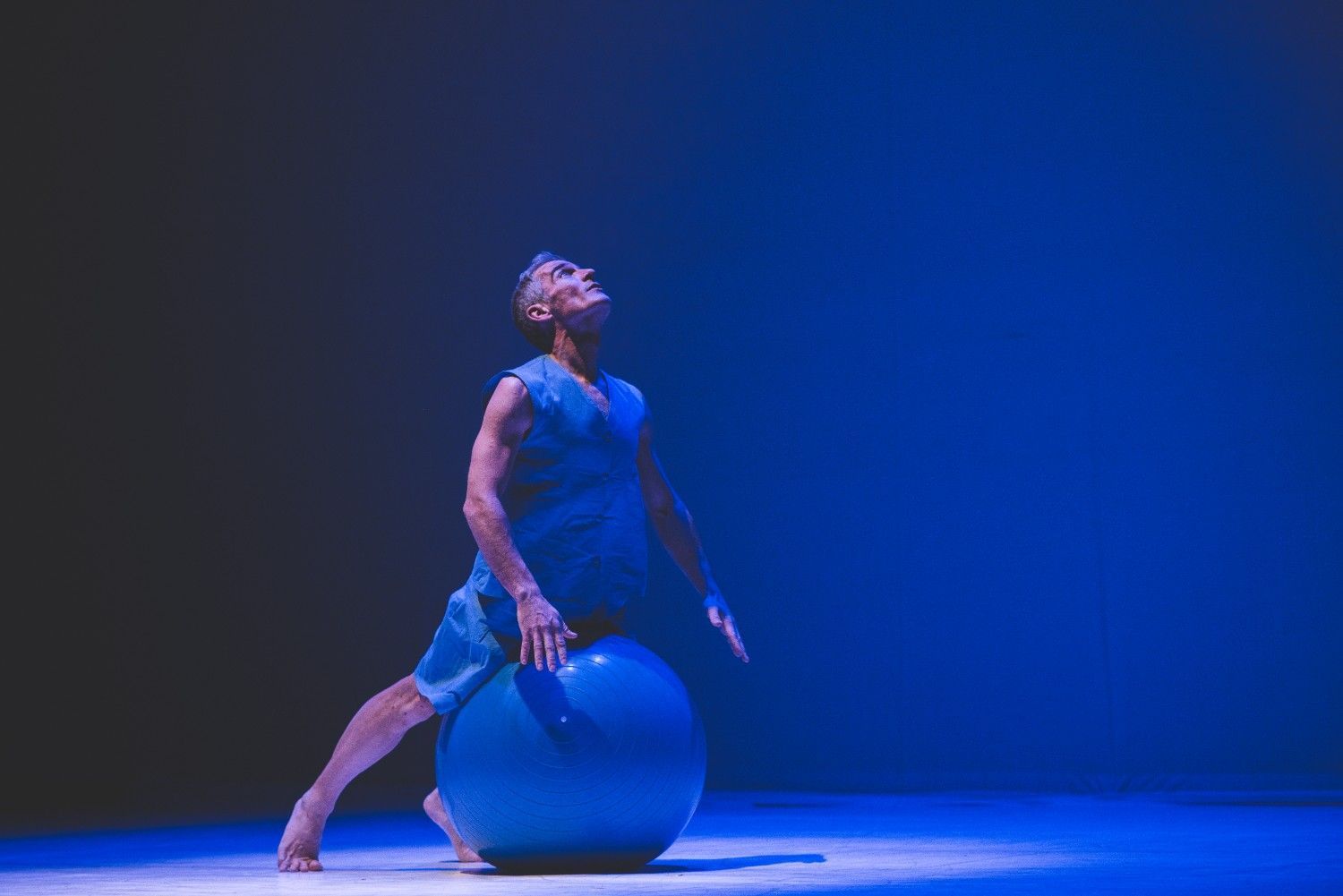 Atleta estirándose sobre una pelota de ejercicio azul bajo una espectacular iluminación azul de escenario.