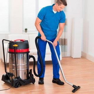 Persona con uniforme azul aspirando un suelo de madera junto a una aspiradora de trineo