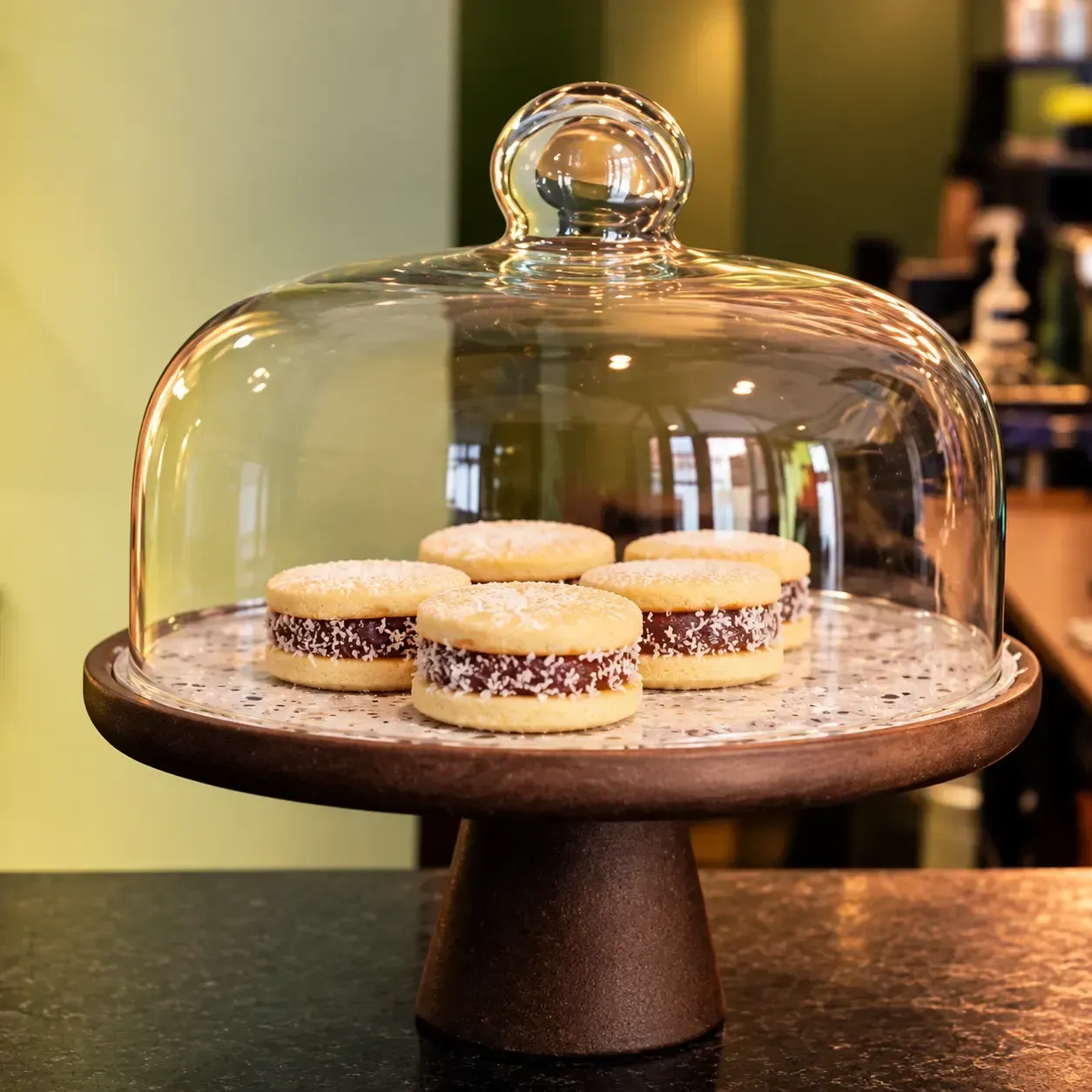 Galletas bajo una campana de cristal, sobre un soporte para tartas en una cafetería.