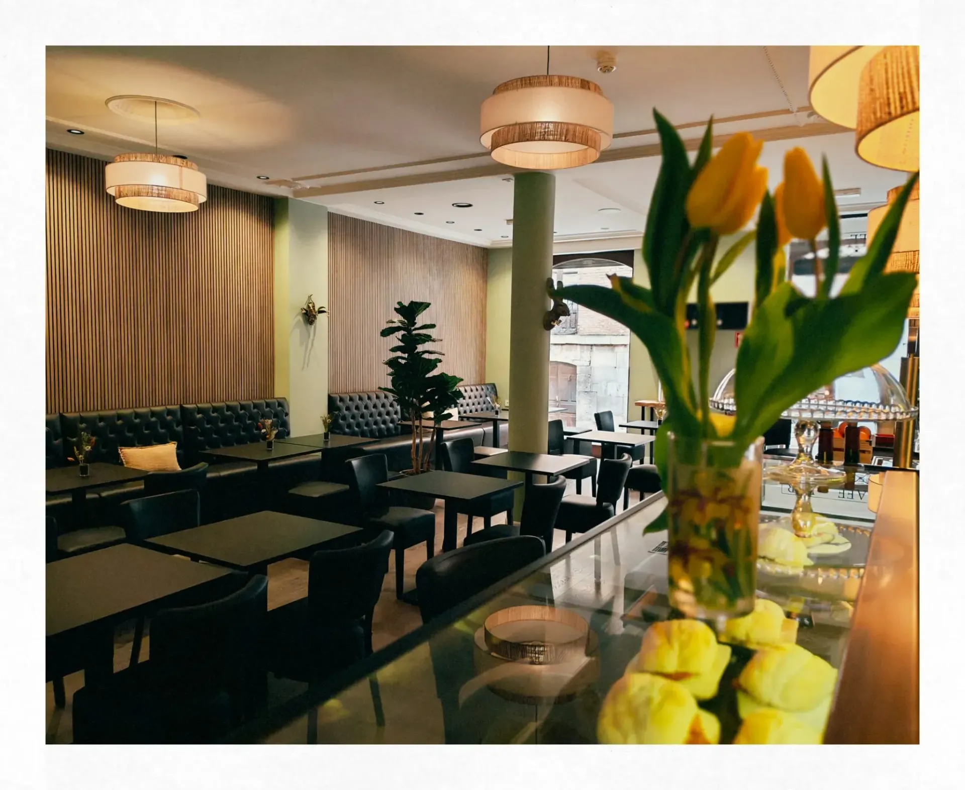 Elegante interior de restaurante con mesas oscuras, lámparas colgantes y flores amarillas en primer plano