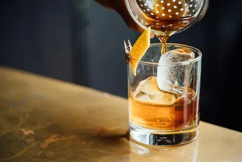Una bebida de color ámbar se cuela en un vaso bajo sobre la barra