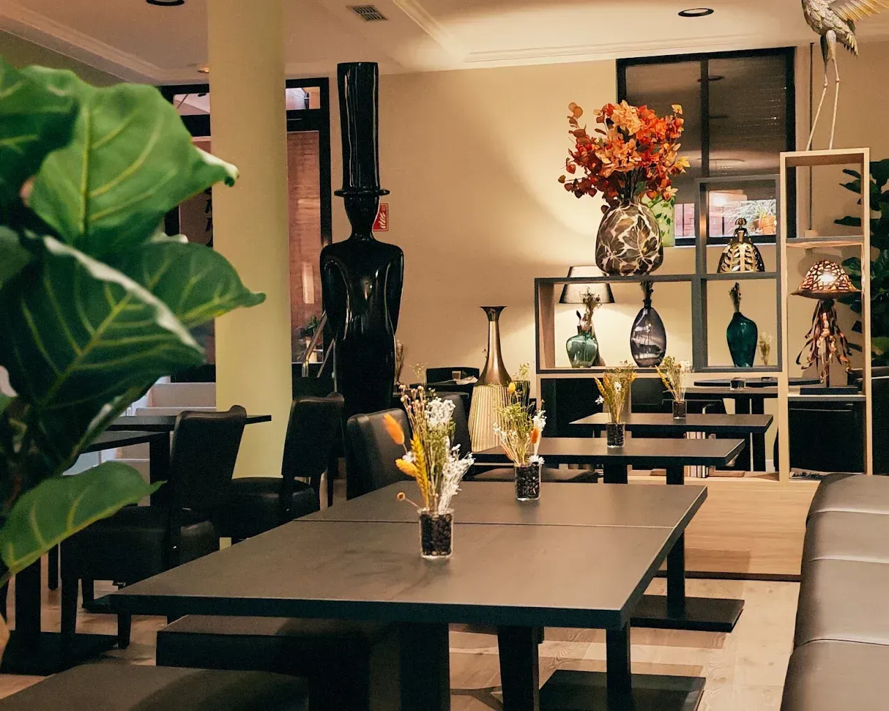 Interior moderno de restaurante, con mesas oscuras, asientos de cuero y jarrones decorativos en las estanterías