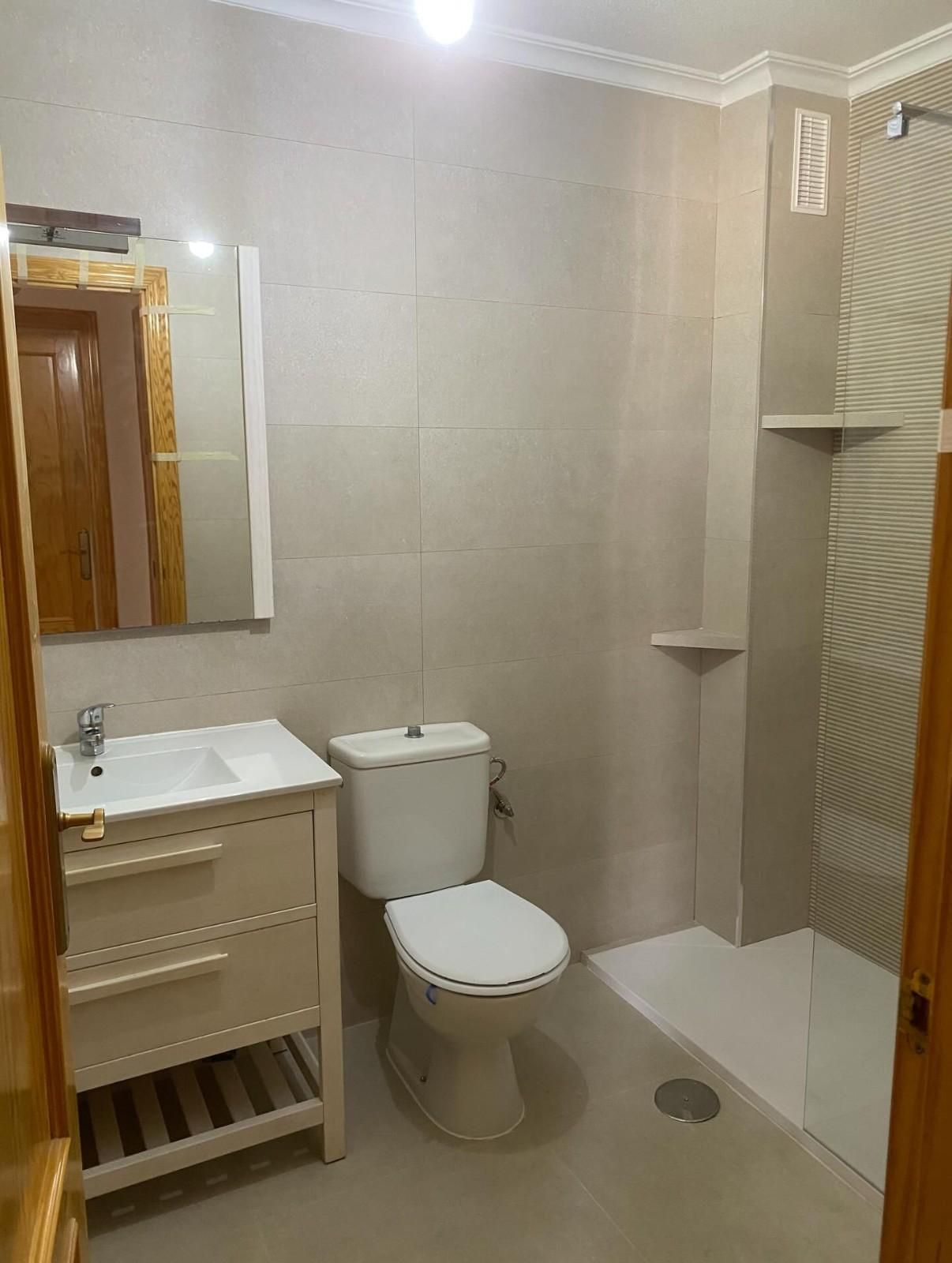 Baño con azulejos beige, inodoro blanco, lavabo y ducha independiente.