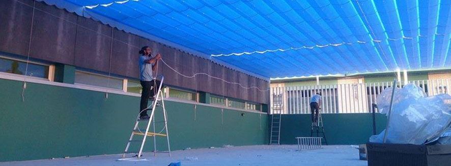 Un hombre está de pie en una escalera pintando el techo de un edificio.