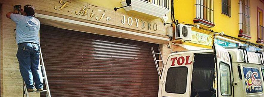 Un hombre en una escalera está trabajando en un edificio al lado de una furgoneta.