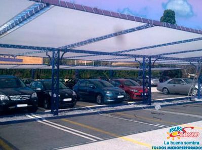Hay muchos coches aparcados bajo un toldo en un estacionamiento.