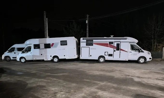 Dos autocaravanas blancas aparcadas una al lado de la otra por la noche en un terreno de tierra.