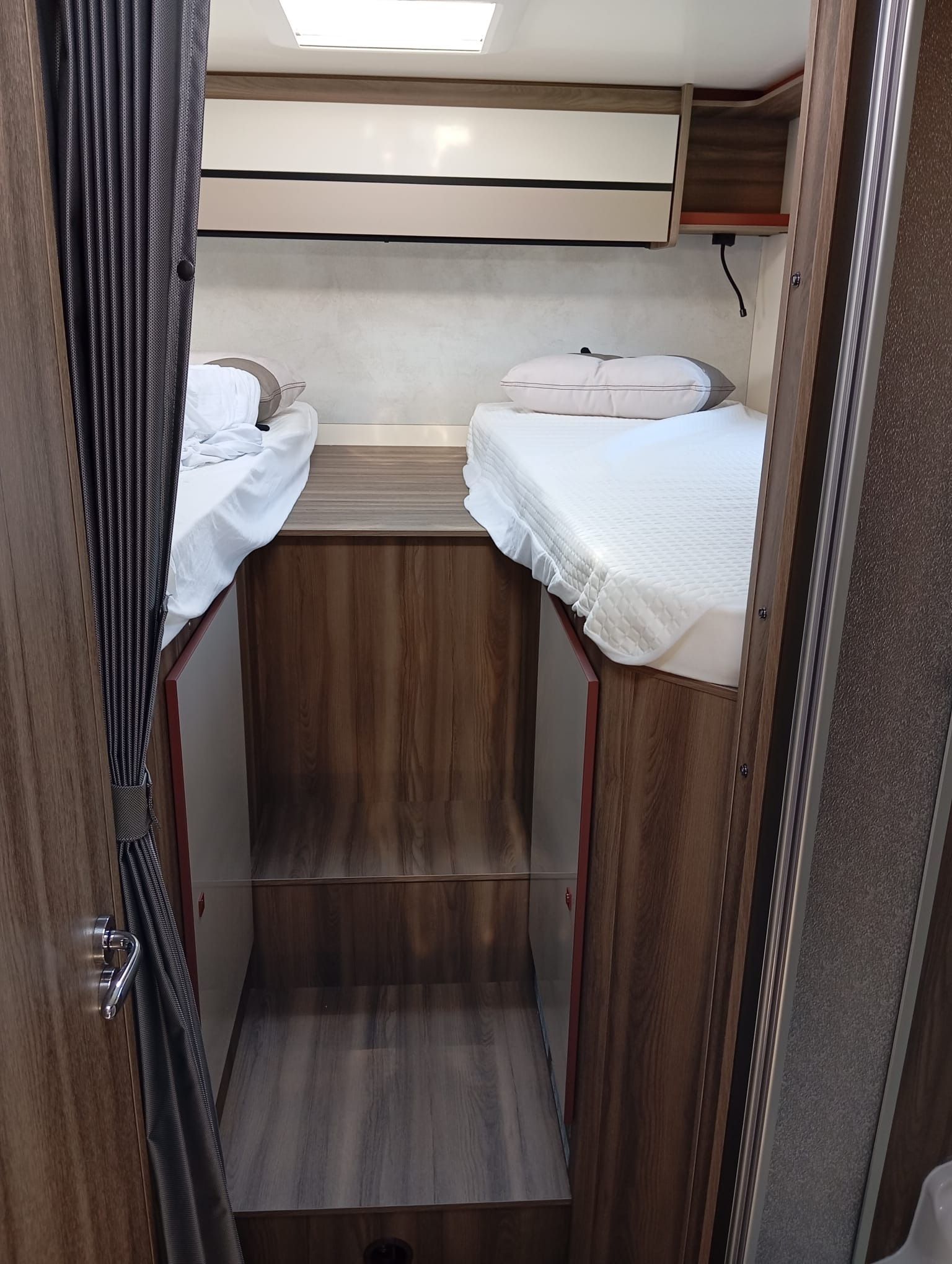 Cabaña pequeña con dos camas individuales, armarios de madera y un estrecho pasillo central.