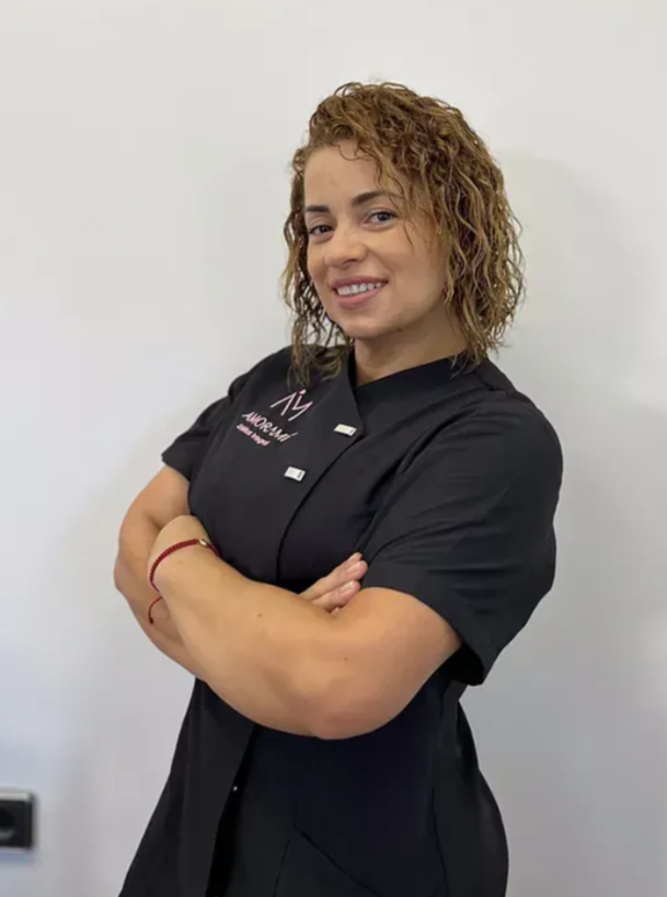 Mujer con cabello rizado, brazos cruzados, vistiendo uniforme negro, sonriendo.