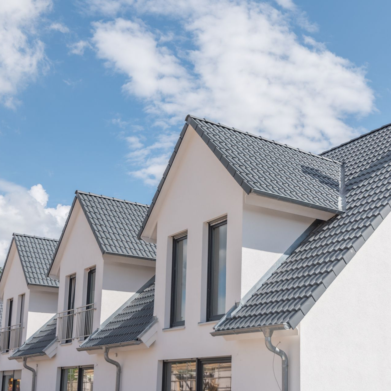 Rangée de maisons blanches aux toits de tuiles grises se détachant sur un ciel bleu nuageux.