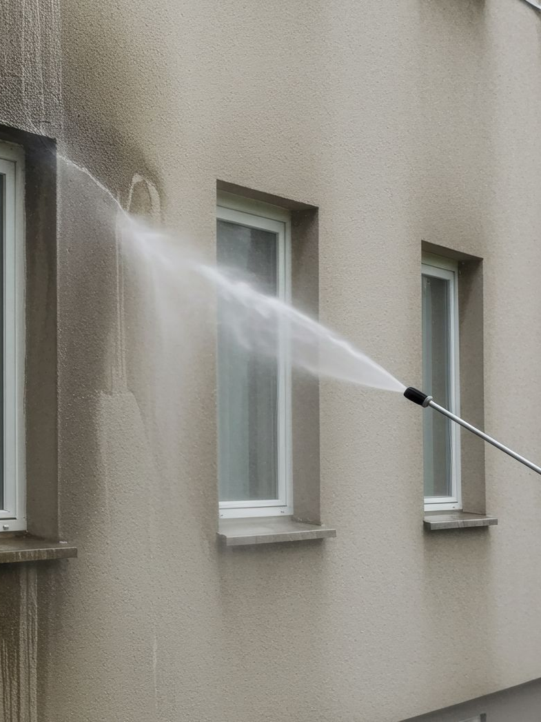 Nettoyage à haute pression de la façade d'un bâtiment beige aux fenêtres à cadre blanc.