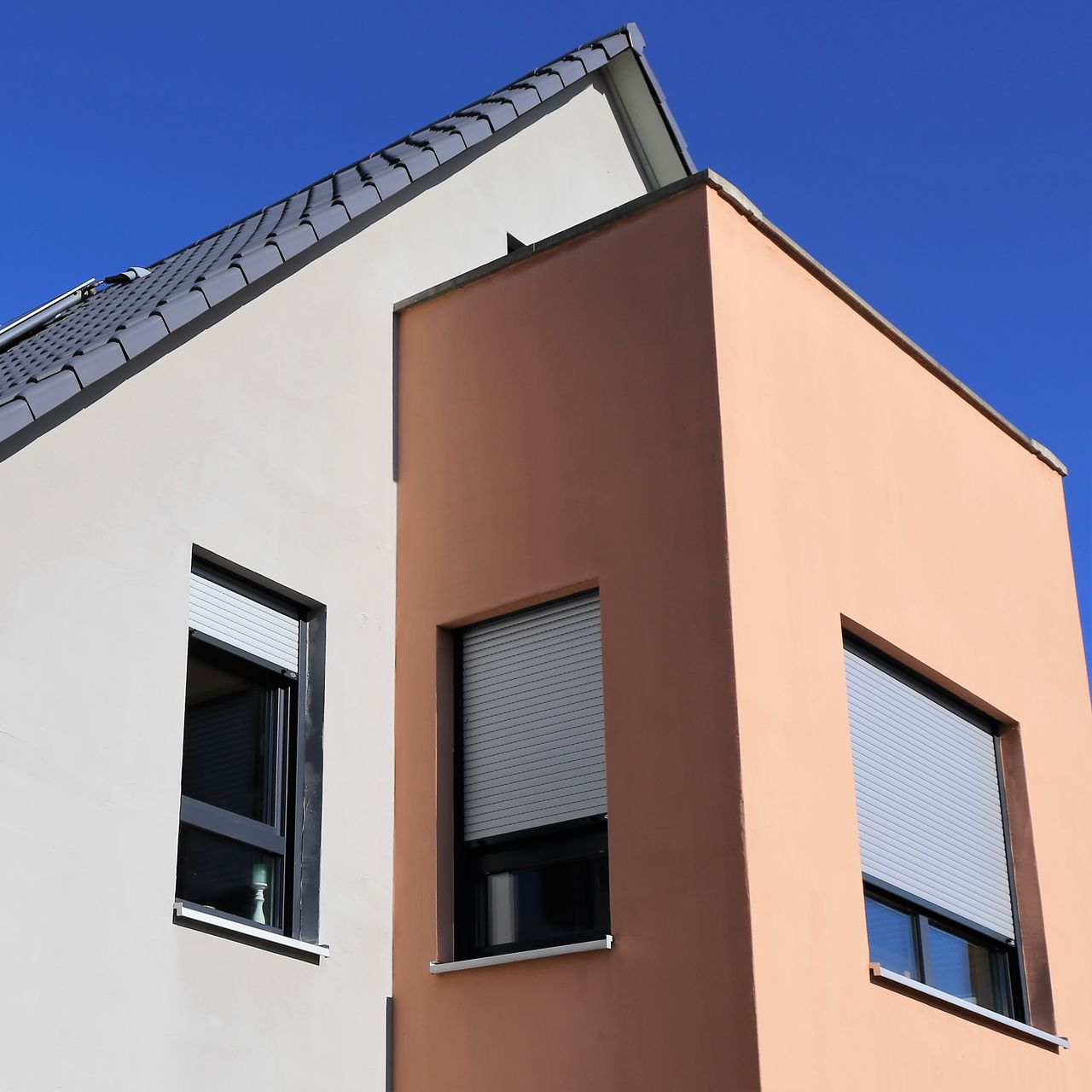 Extérieur de bâtiment moderne avec murs blancs et pêche, fenêtres sombres et ciel bleu.