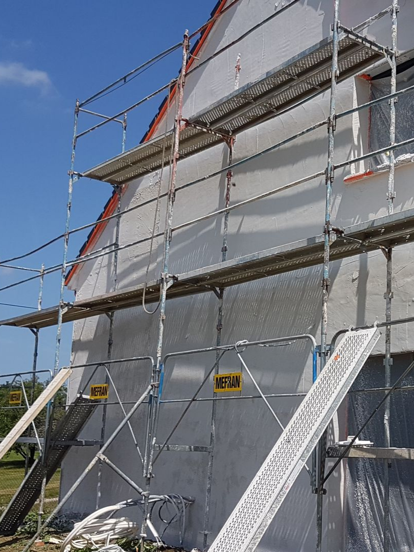 Échafaudage installé sur le côté d'une maison en construction. Le mur est blanc et le toit rouge. Ciel bleu en arrière-plan.