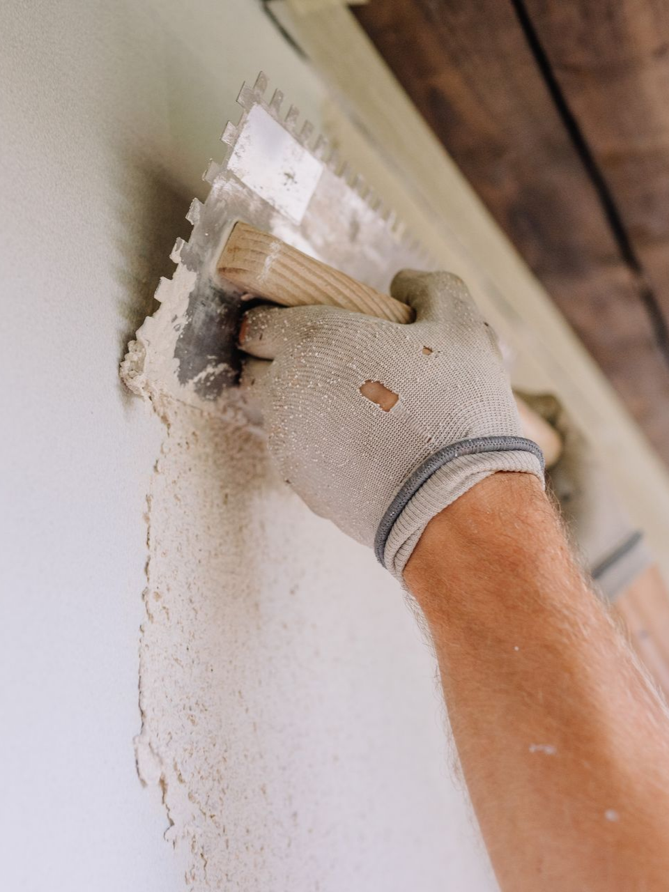 Main gantée lissant du plâtre sur un mur à l'aide d'une truelle.