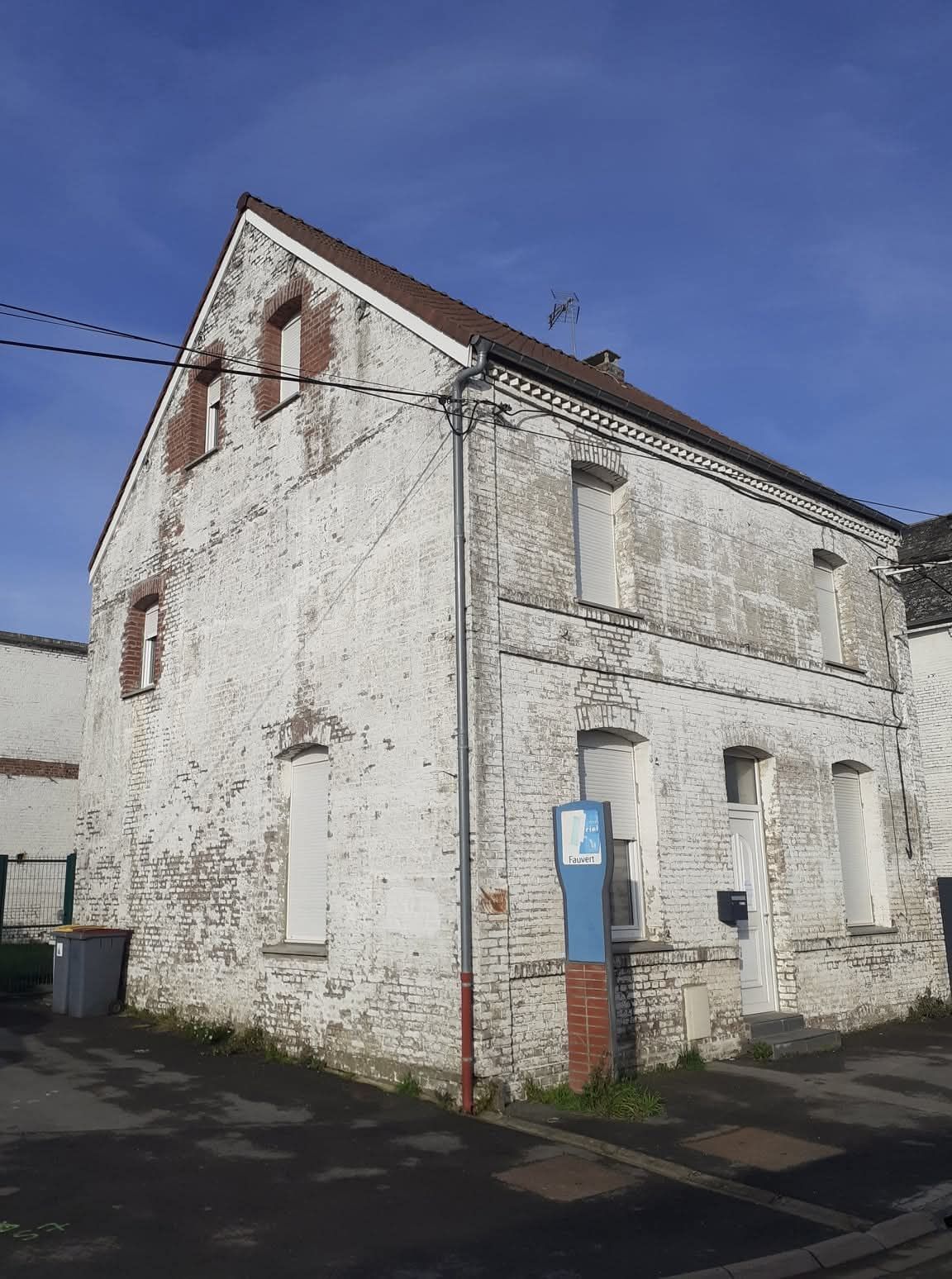 Bâtiment en briques blanches avec un toit brun et un ciel bleu en arrière-plan.