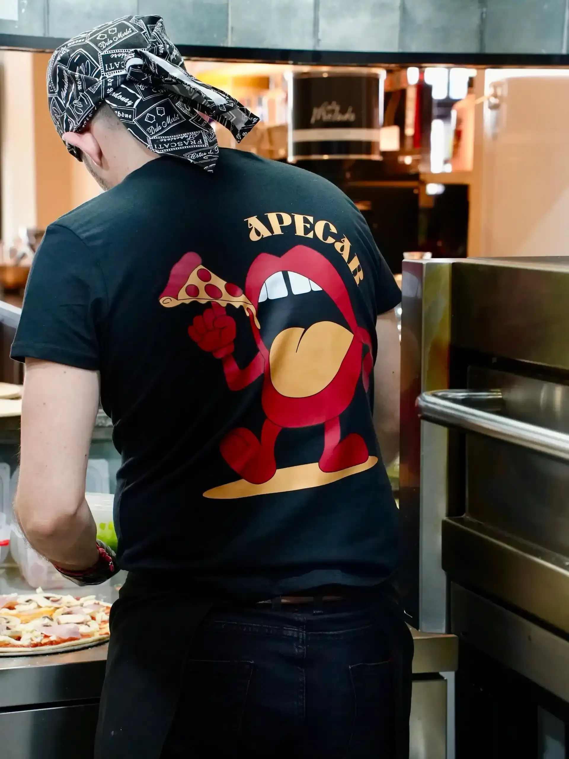 Chef con camiseta negra con gráfico de pizza, cocinando en una cocina.