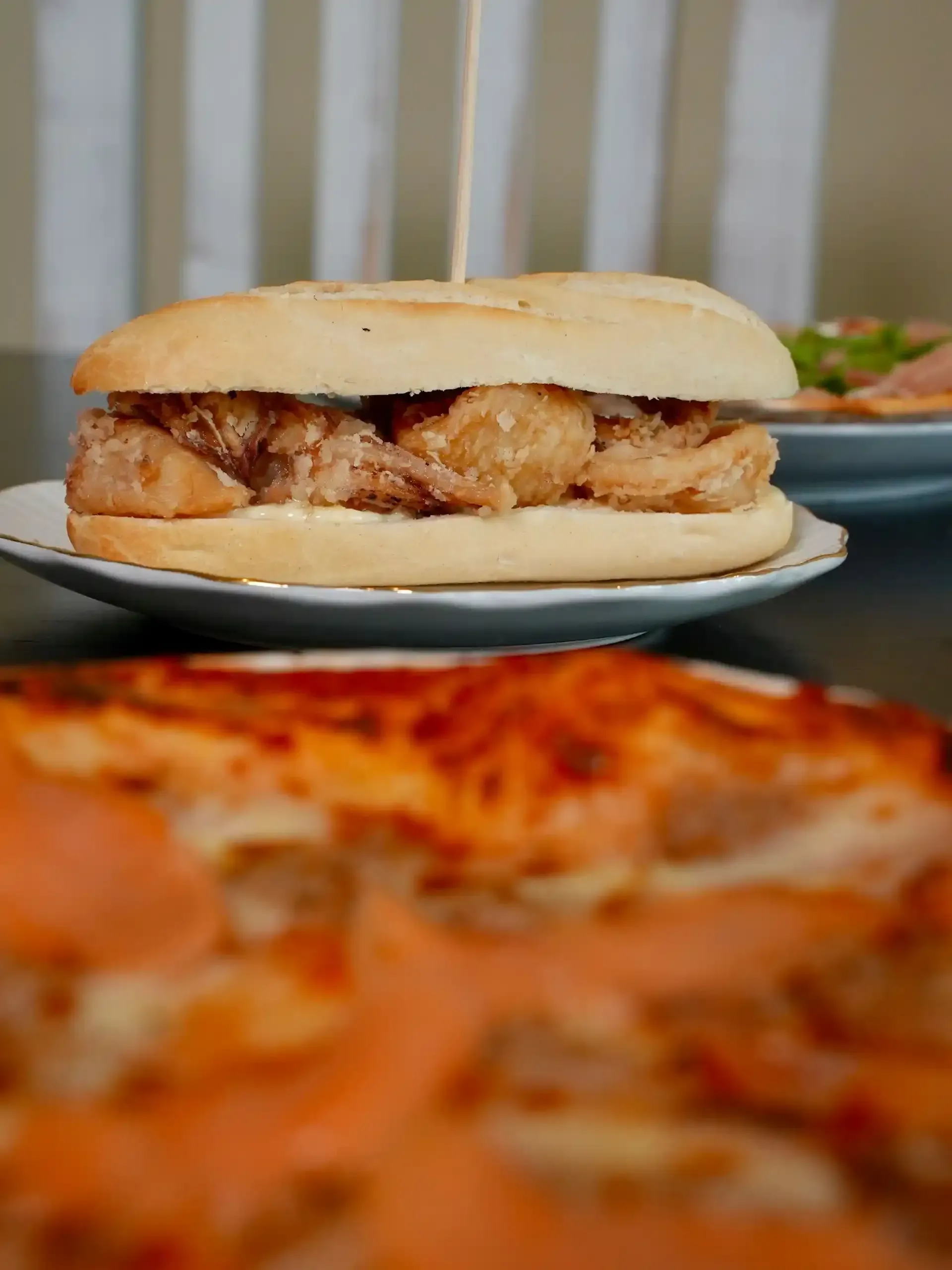 Sándwich de mariscos fritos en un plato con un primer plano borroso de comida y fondo rayado.