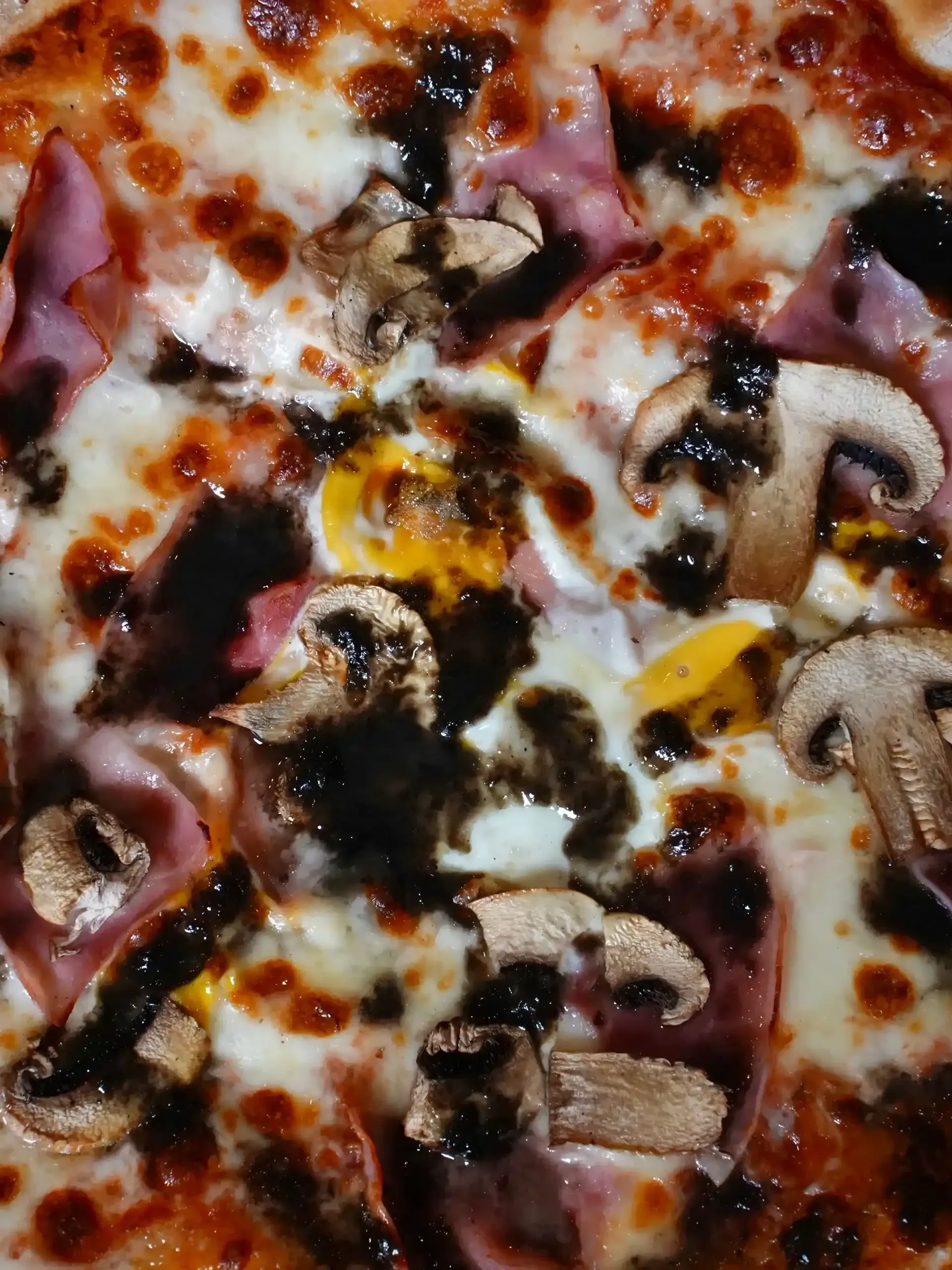 Pizza con champiñones, jamón, queso y una salsa oscura rociada por encima.