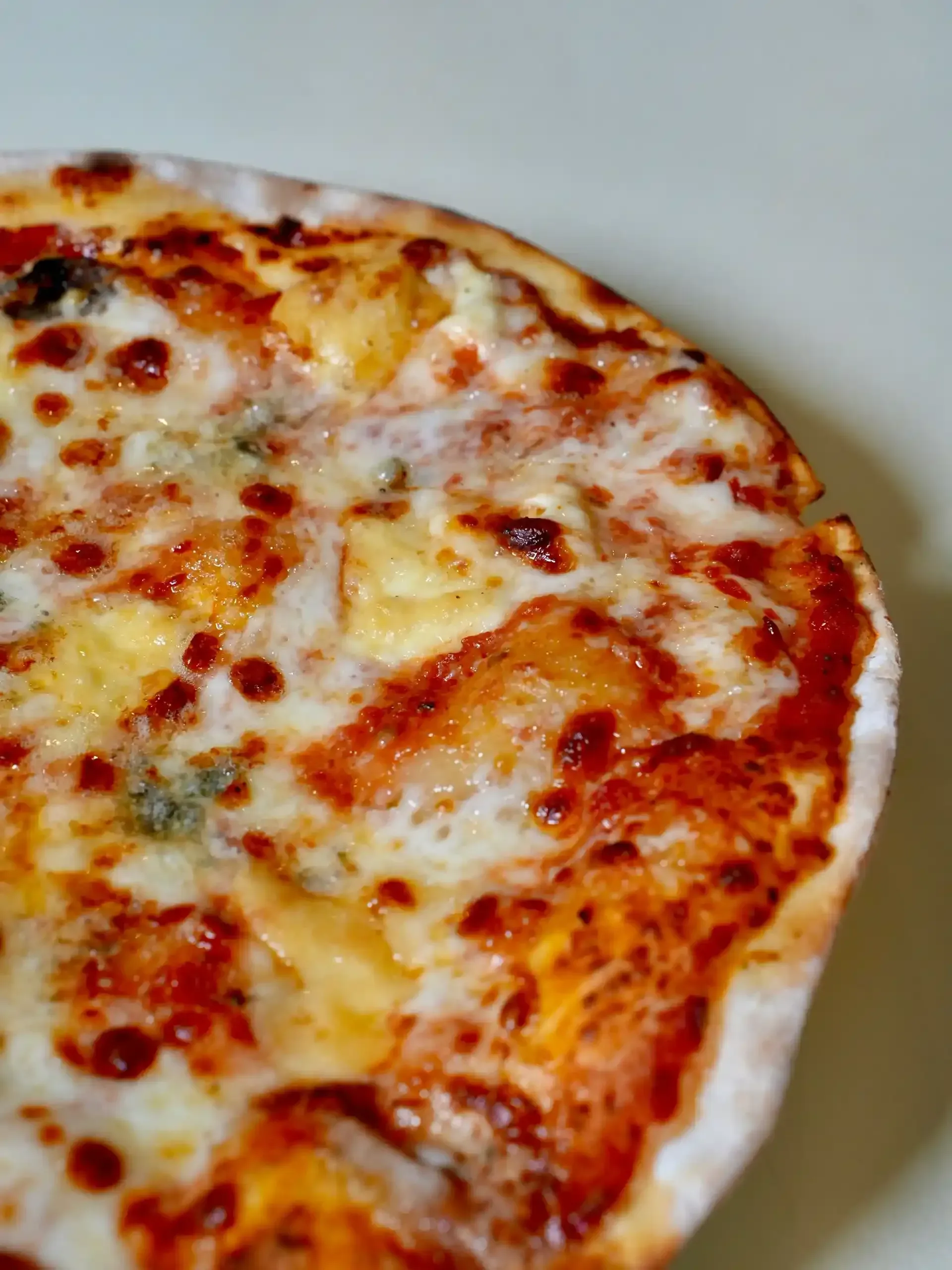 Primer plano de una pizza con queso derretido, salsa de tomate y una corteza ligeramente carbonizada.