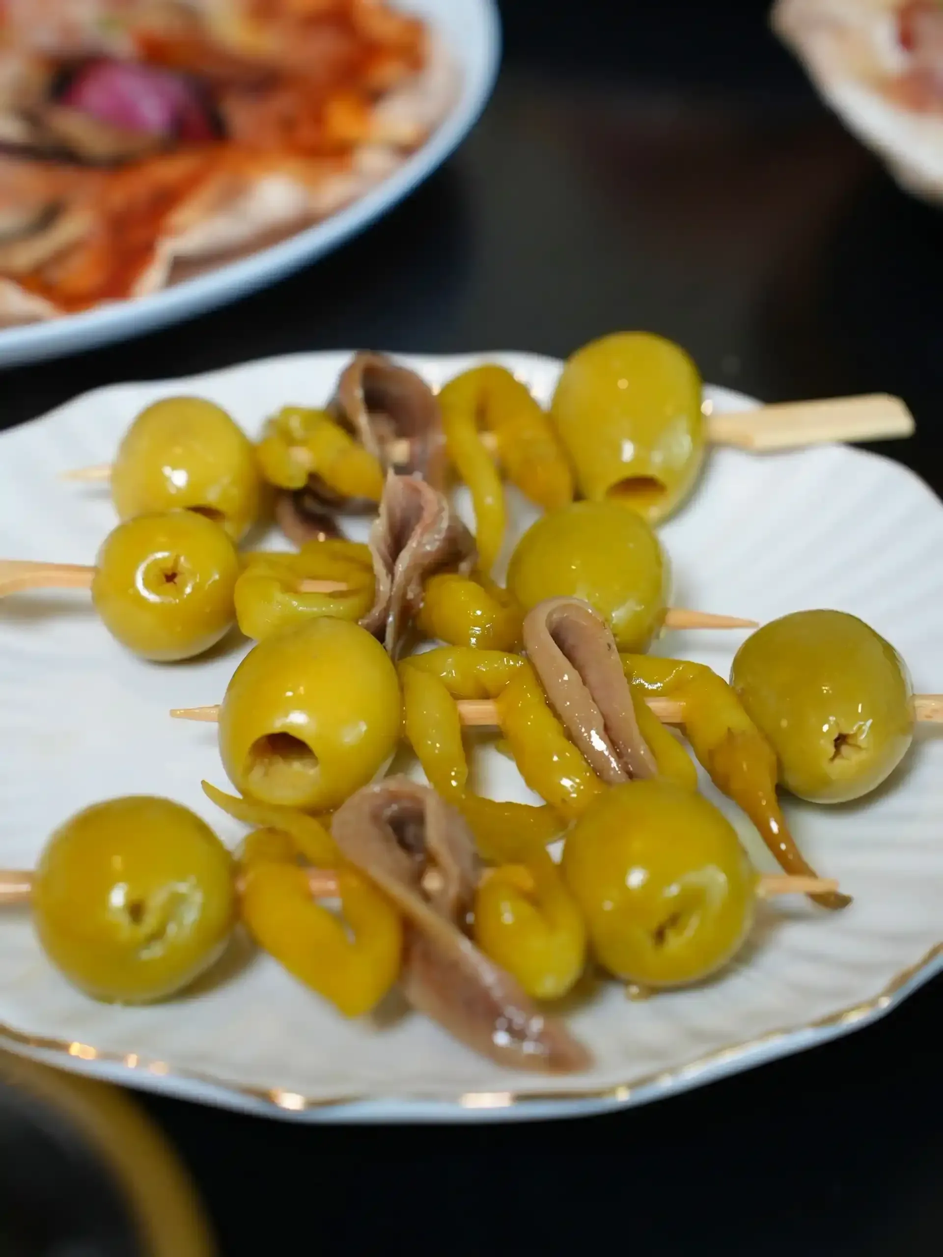 Aperitivo de aceitunas, pimiento y anchoa en brocheta en un plato blanco.
