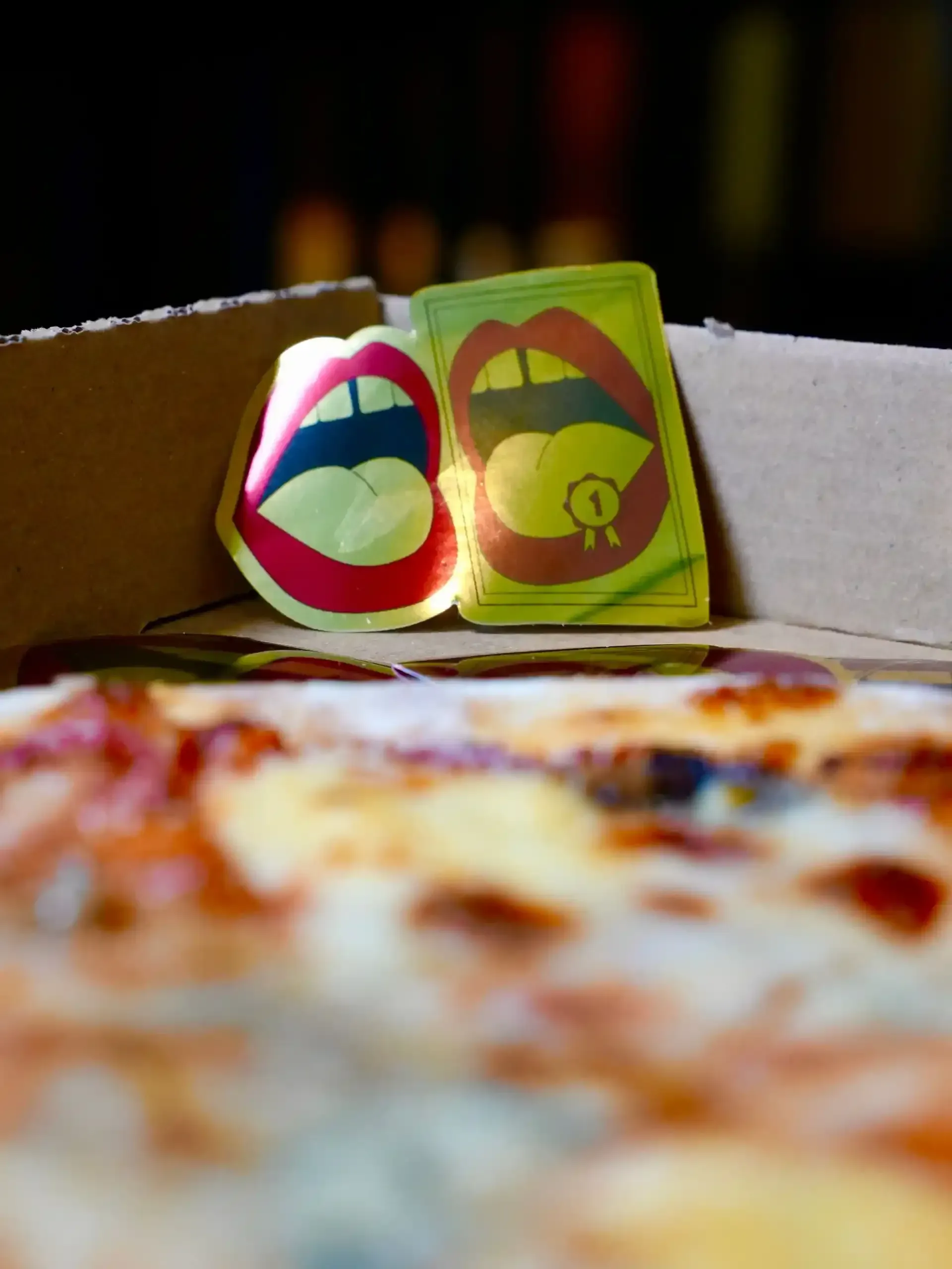 Dos bocas de dibujos animados en una caja de pizza con una pizza en primer plano; una tiene una medalla.