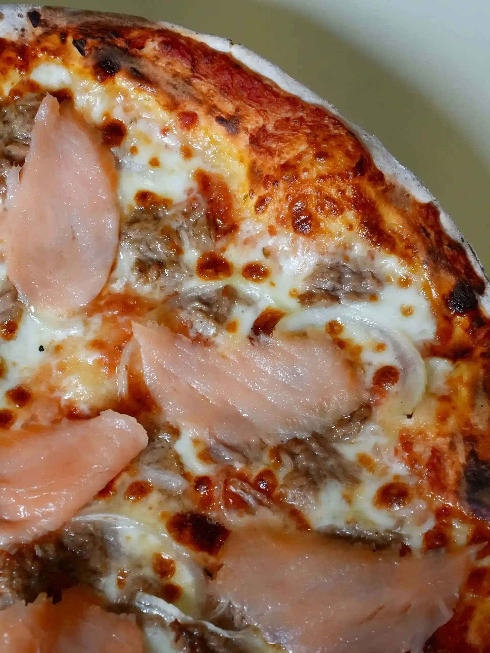 Pizza cubierta con salmón y queso derretido.