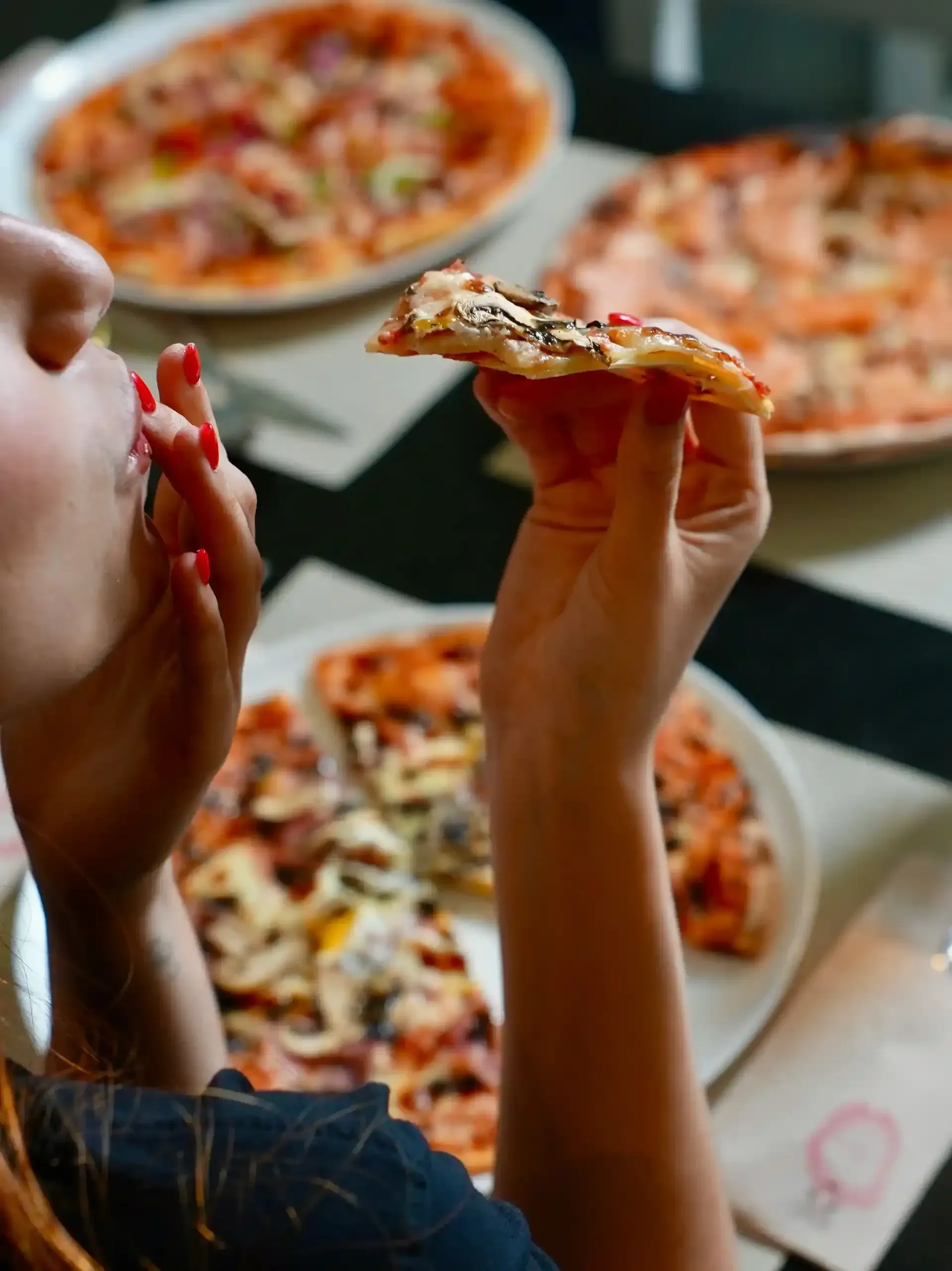 Persona comiendo una porción de pizza de una mesa con otras pizzas.