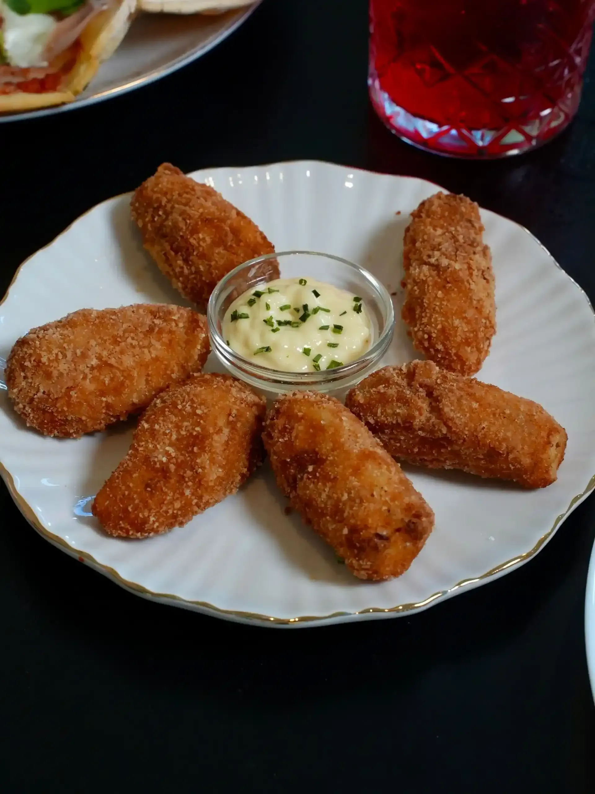 Croquetas fritas dispuestas alrededor de un pequeño recipiente con salsa en un plato blanco.