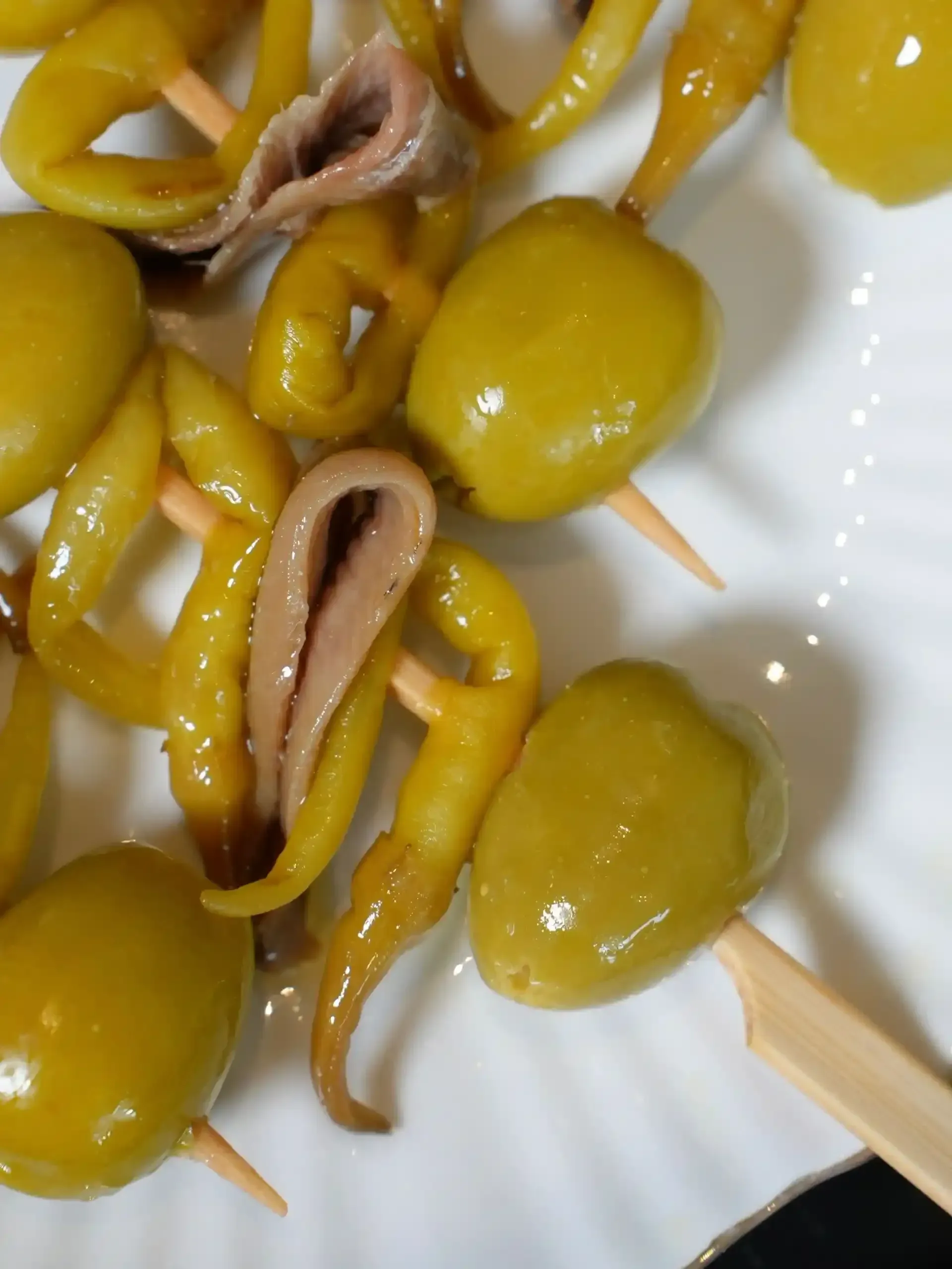 Brochetas de aceitunas verdes, pimientos encurtidos y anchoas en un plato blanco.