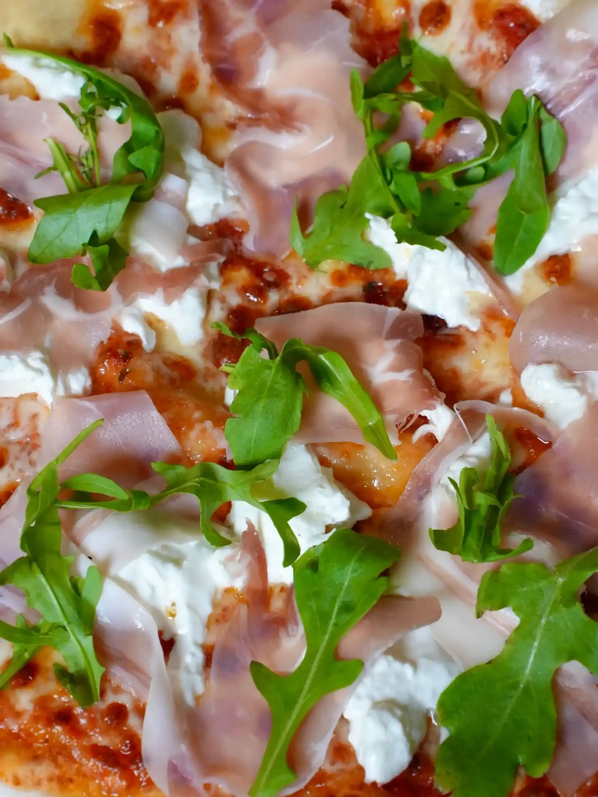 Pizza cubierta con prosciutto, queso ricotta y rúcula.