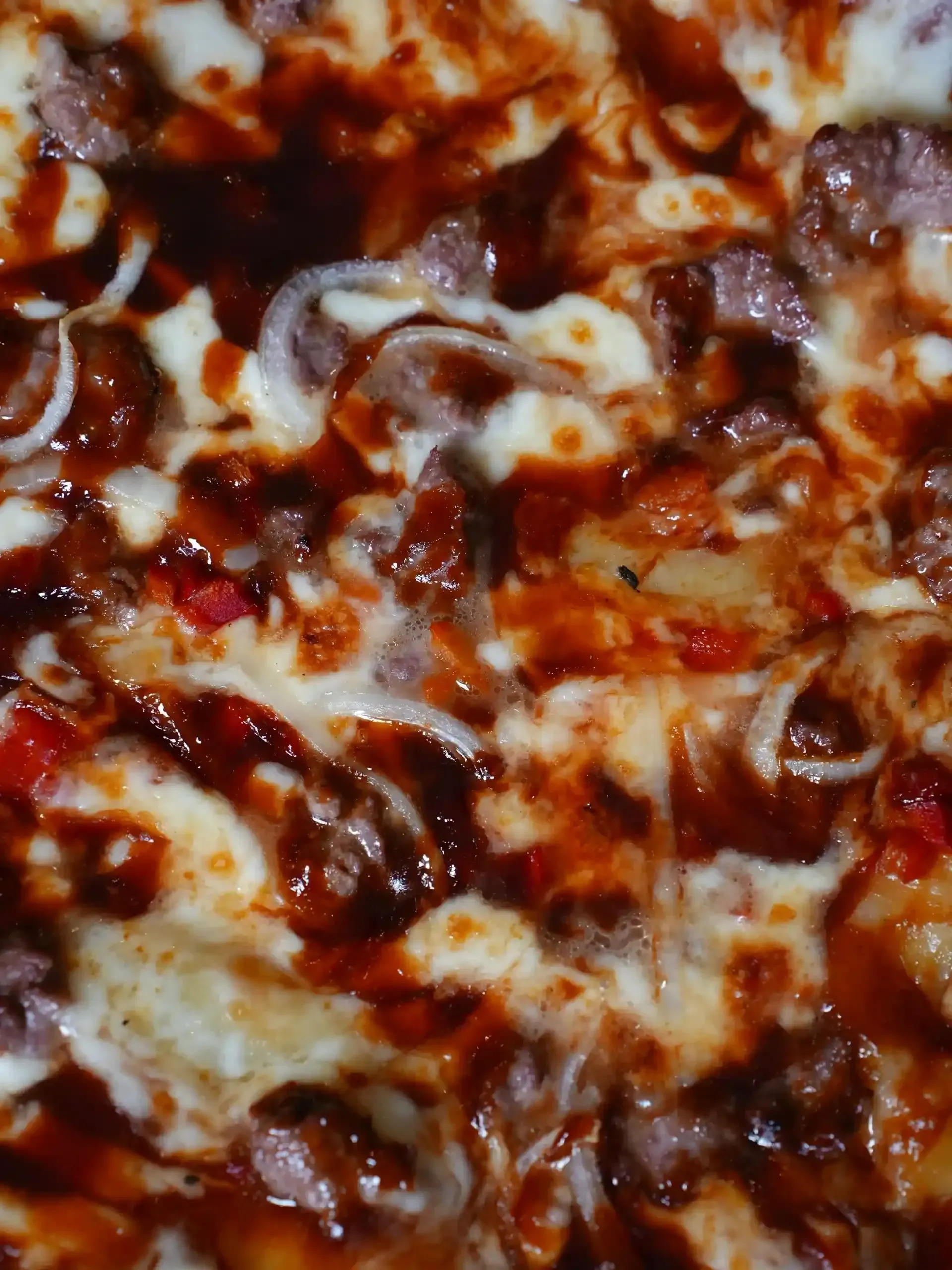 Pizza con carne, cebolla y salsa, cubierta de queso derretido.