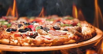 Una pizza está colocada en una bandeja de madera encima de una estufa de leña.