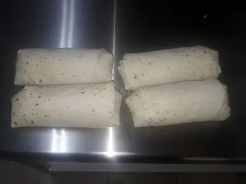 Cuatro burritos están sentados encima de un mostrador de acero inoxidable.