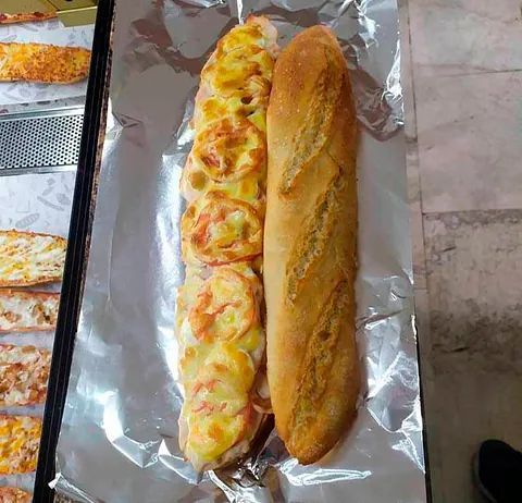 Una baguette larga cubierta de queso y tomates envuelta en papel de aluminio.