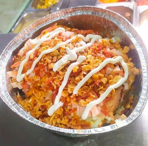 Un recipiente de papel de aluminio lleno de comida y salsa sobre una mesa.