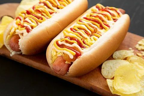 Dos perritos calientes con ketchup y mostaza en una tabla de cortar de madera con patatas fritas.